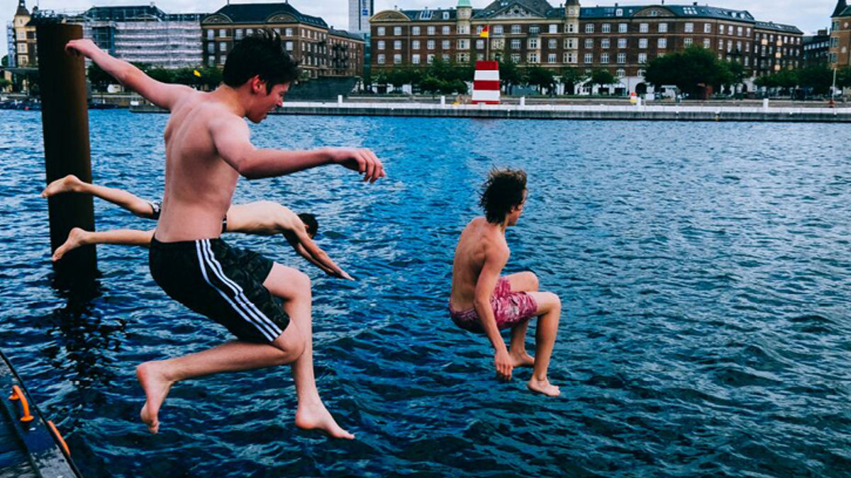 Boys jumping in a river in swim trunks.