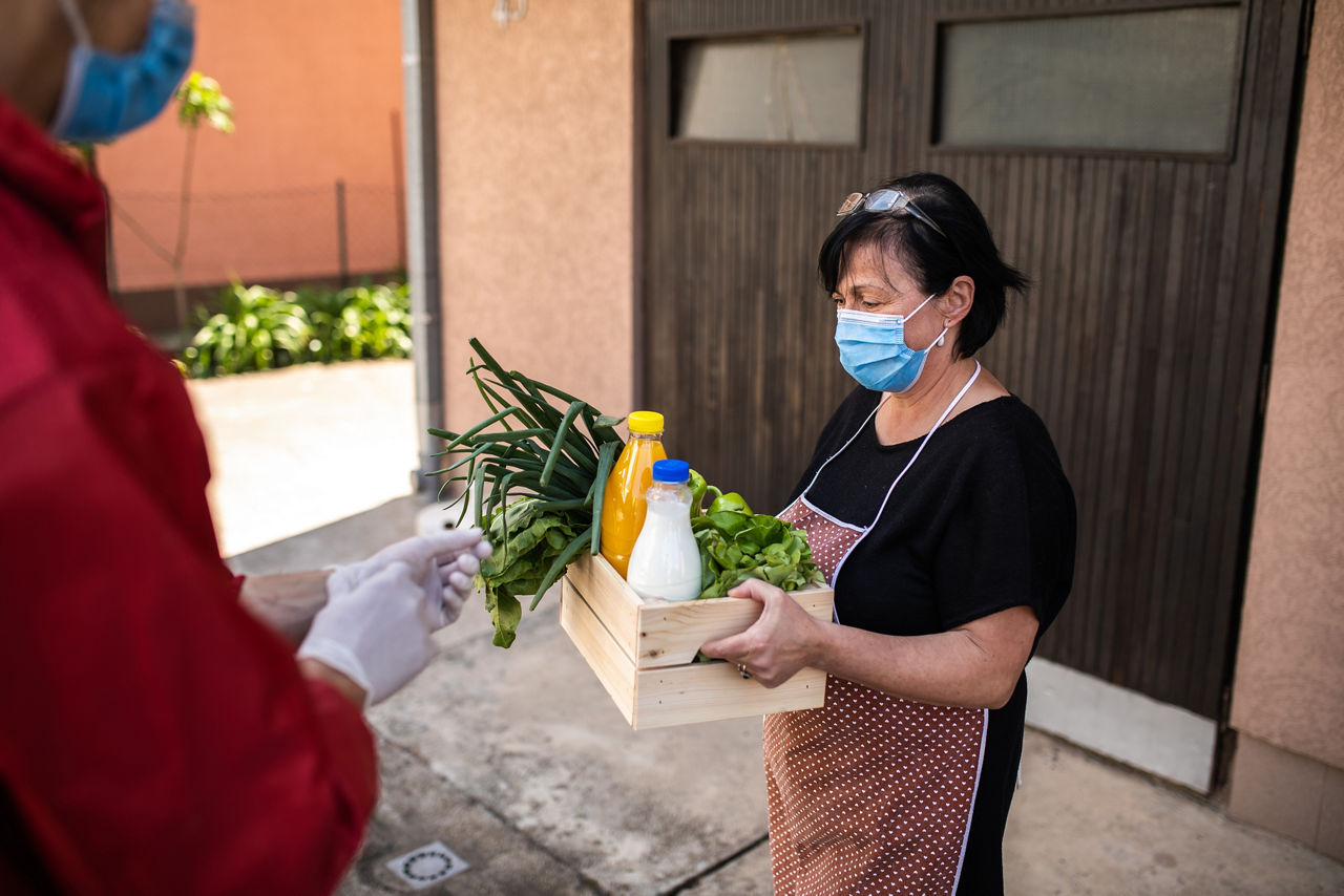 Senior woman wearing protective mask taking groceries from caring volunteer during covid-19 lockdown